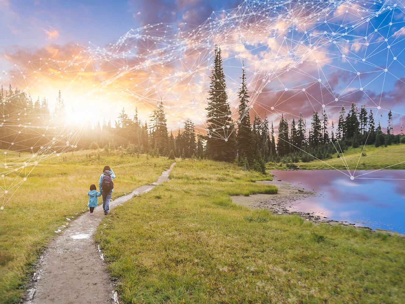 Mother and daughter walking on a trail to the right of a mountain lake. 